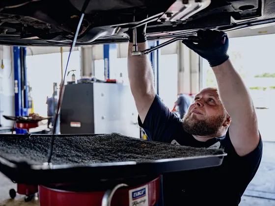 Mechanic working beneath a lifted vehicle above an oil drain pan